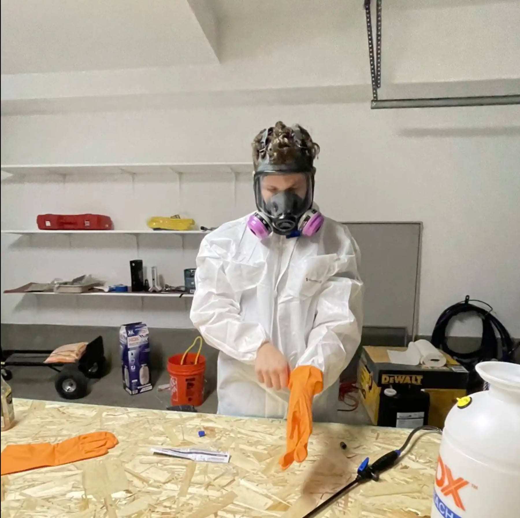 Technician in a protective suit and respirator pulling on gloves at a workbench